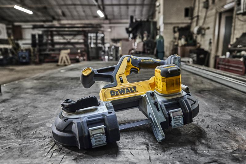 DEWALT cordless band saw (model DCS378N) placed on a workbench in an industrial workshop, with various tools and machinery in the background.