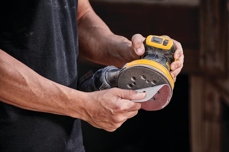 Close-up of a person attaching sanding paper to a DEWALT cordless random orbital sander.