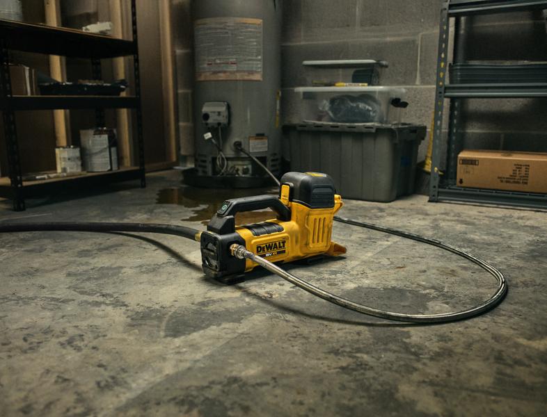 A yellow and black DEWALT portable cordless water transfer pump (model DCE050N) with attached hose is placed on a concrete floor in a workshop or utility room, surrounded by shelves and storage containers.