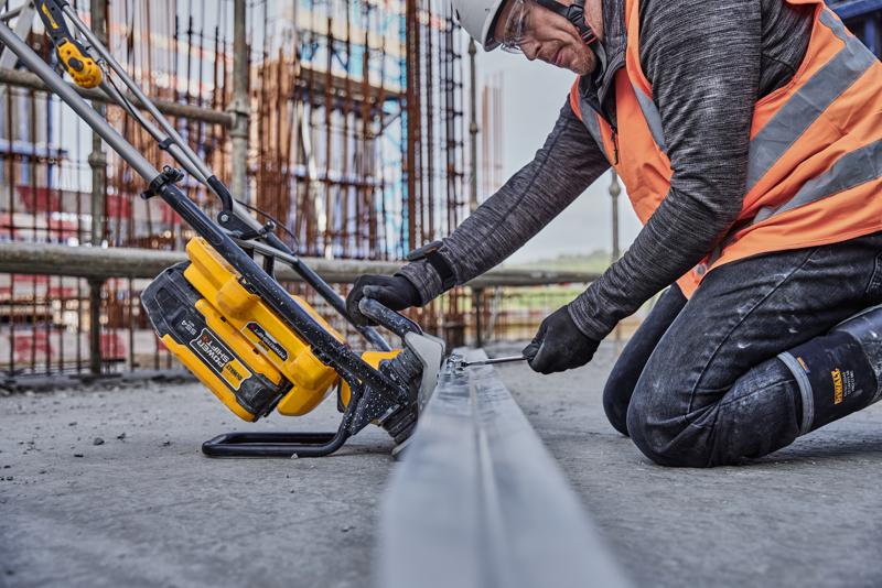 A person wearing construction safety gear uses a DEWALT cordless power tool (SKU: DCPS330N) on a metal beam at a construction site.
